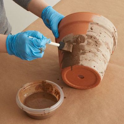 a person in blue gloves is painting a pot with brown paint on the ground next to a white container