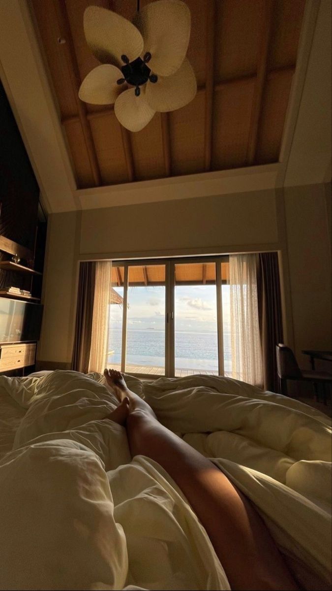 a person laying on a bed in front of a window with the ocean out side