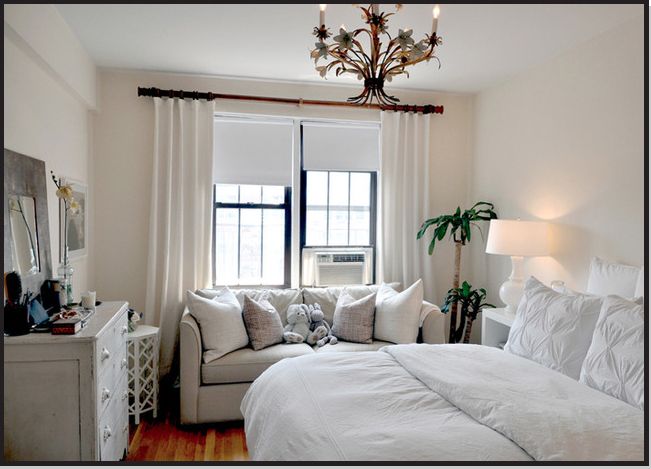 a white bed sitting in a bedroom next to a window covered in pillows and blankets