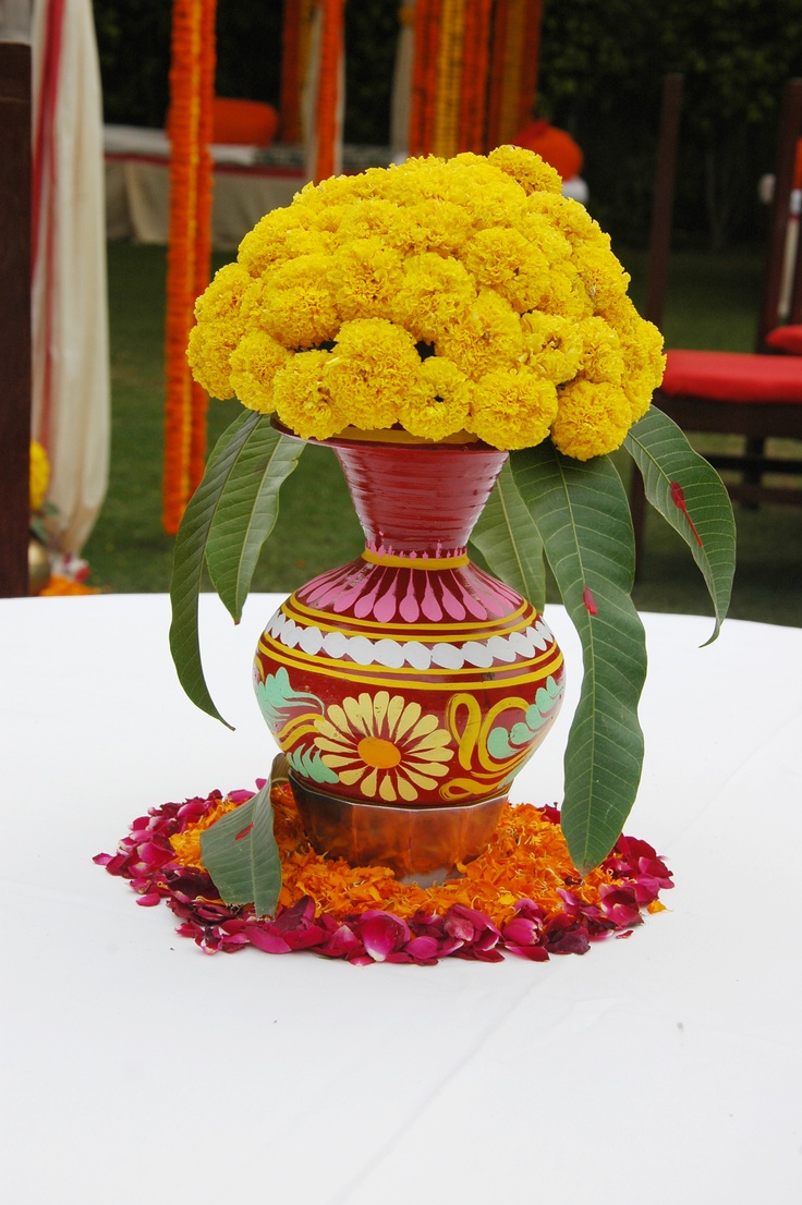 a vase filled with yellow flowers sitting on top of a white table covered in petals