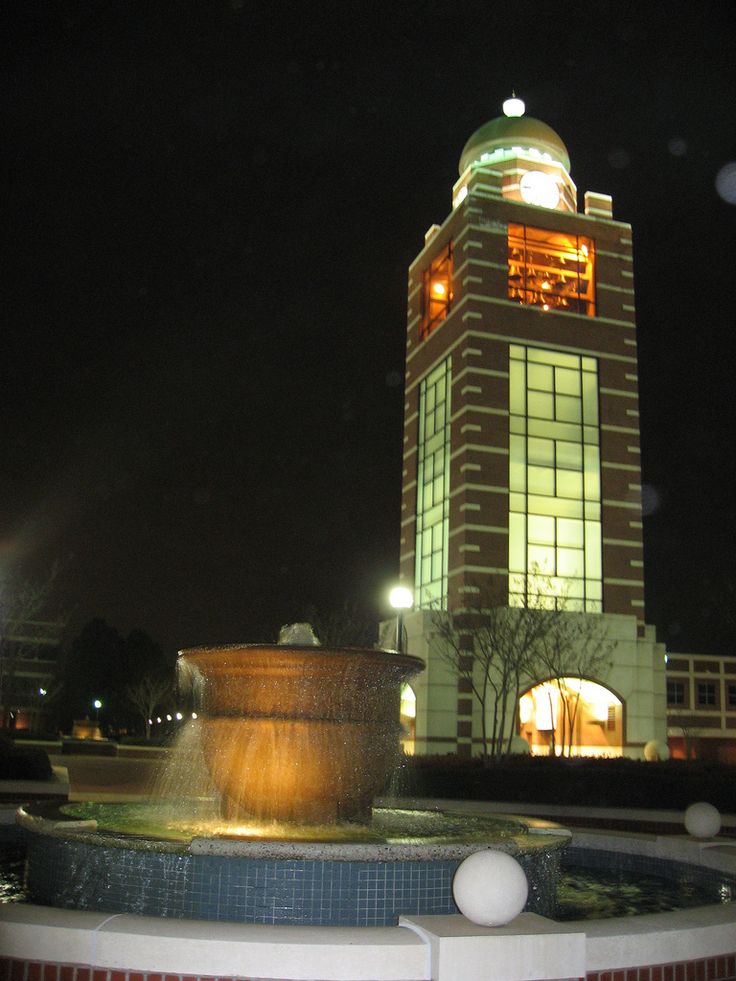 a fountain in front of a building at night with lights shining on the top and below it