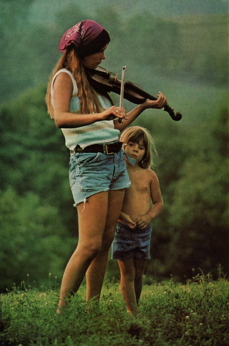 a woman holding a violin while standing next to a little boy on top of a hill