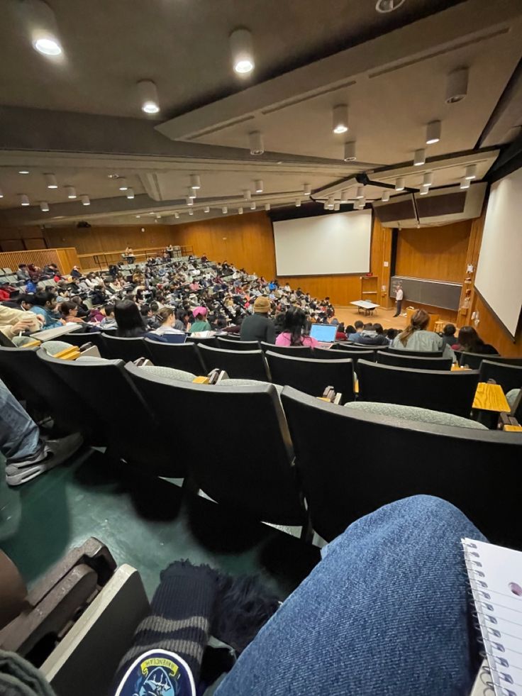 an auditorium with people sitting in seats and on the floor watching a presentation or lecture