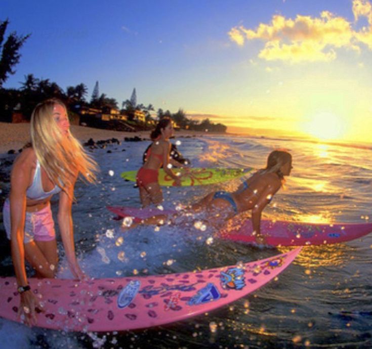 three girls on surfboards in the ocean at sunset