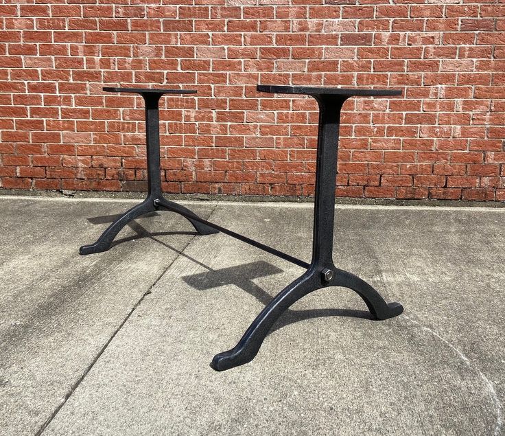 two black metal tables sitting on top of a sidewalk next to a brick wall in front of a building