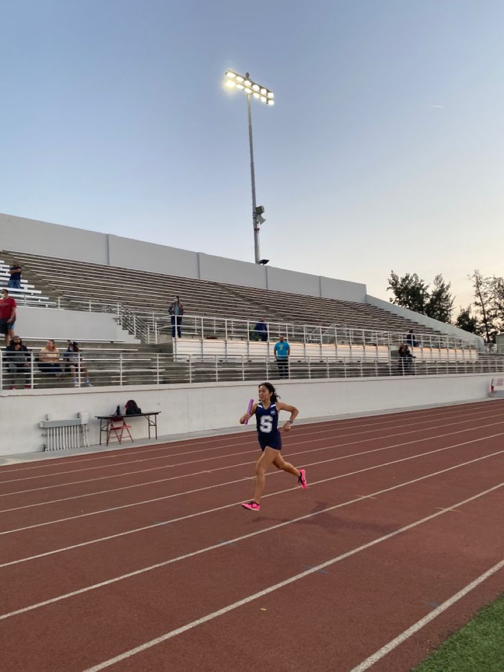 a woman running on a track in front of an empty bleachers at sunset