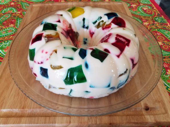 a bundt cake with white icing and colorful toppings on a wooden platter