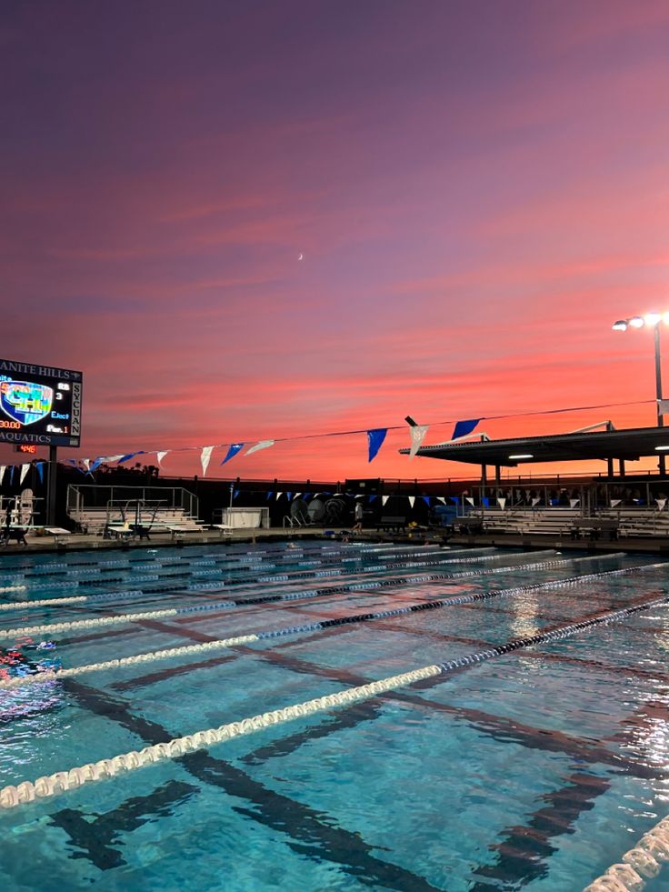 an empty swimming pool with flags flying in the air at sunset or dawn, and people watching from the sidelines