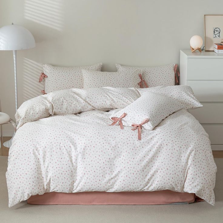 a bed with white sheets and pink bows on the comforter, next to a lamp