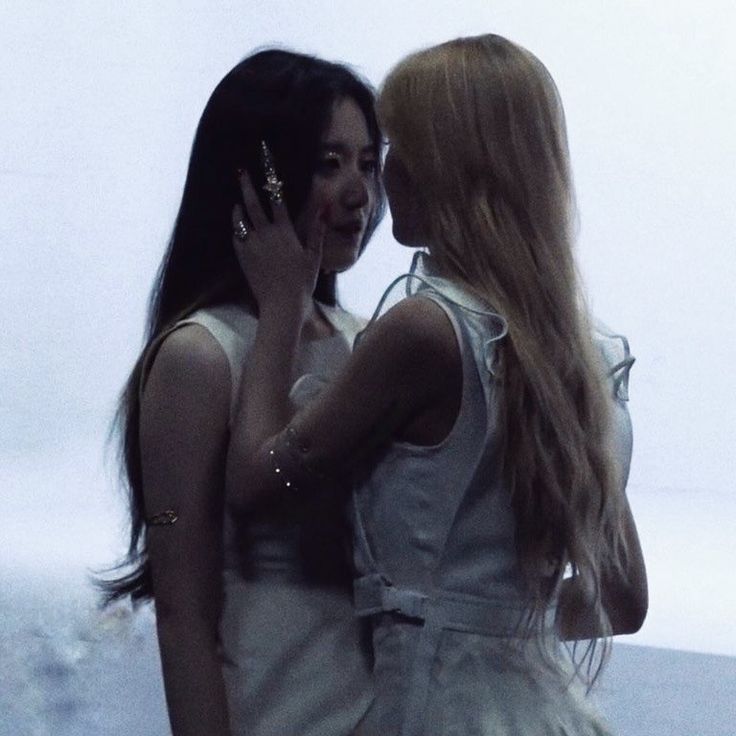 two women standing next to each other in front of a white wall talking on their cell phones