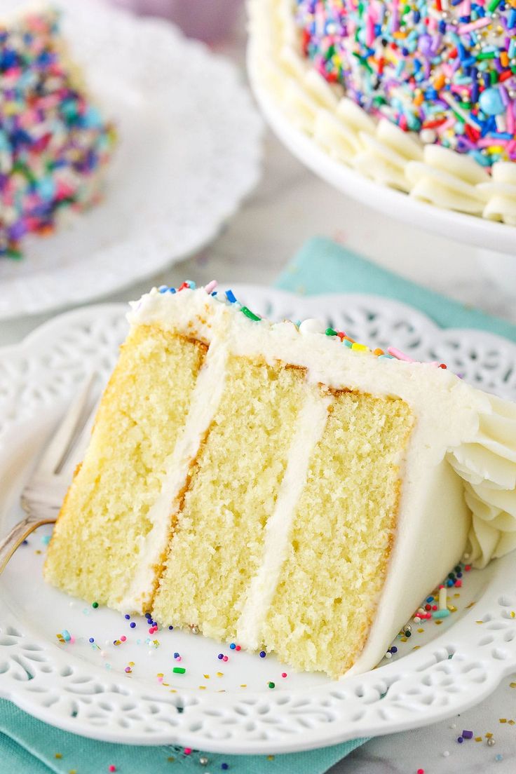 a slice of cake with white frosting and sprinkles sits on a plate