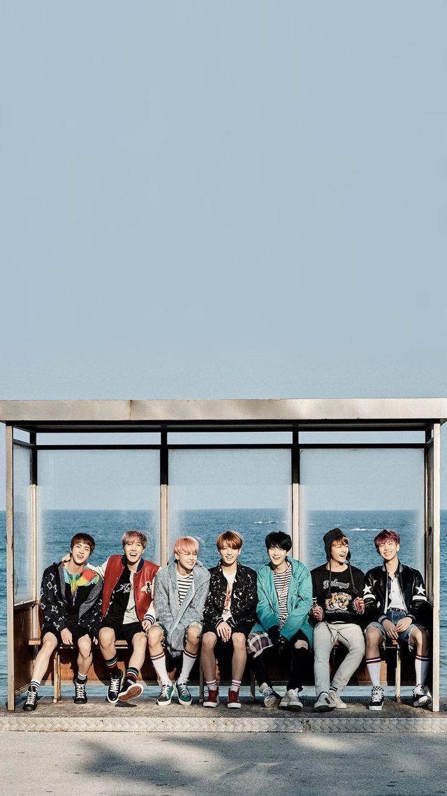 a group of young men sitting on top of a bench near the ocean under a blue sky