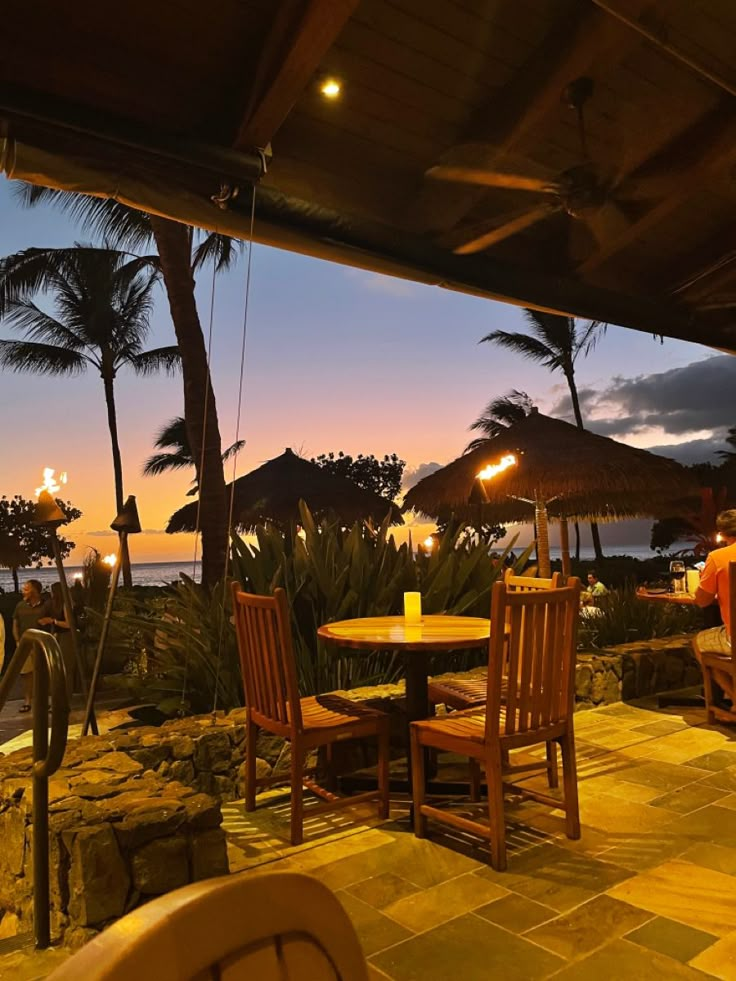 an outdoor dining area with umbrellas and chairs at dusk, overlooking the water's edge