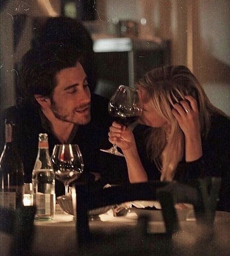 a man and woman sitting at a table with wine glasses in front of their faces