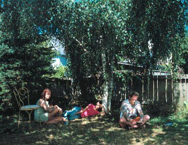 three people sitting in the shade under some trees