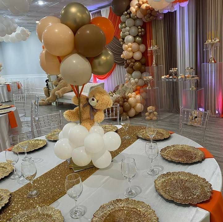 a teddy bear sitting on top of a table surrounded by balloons and other decorations at a party