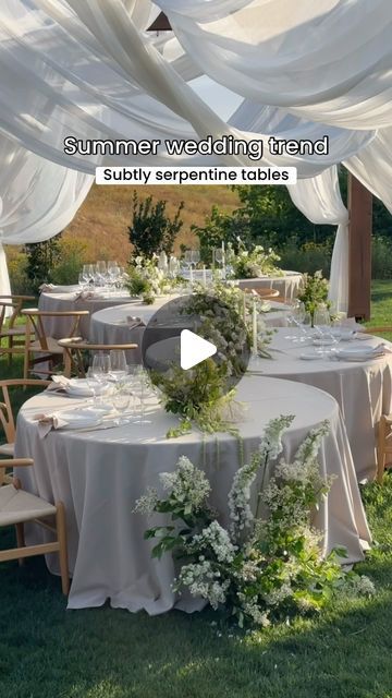 a table set up with white linens and greenery for a wedding reception in the grass