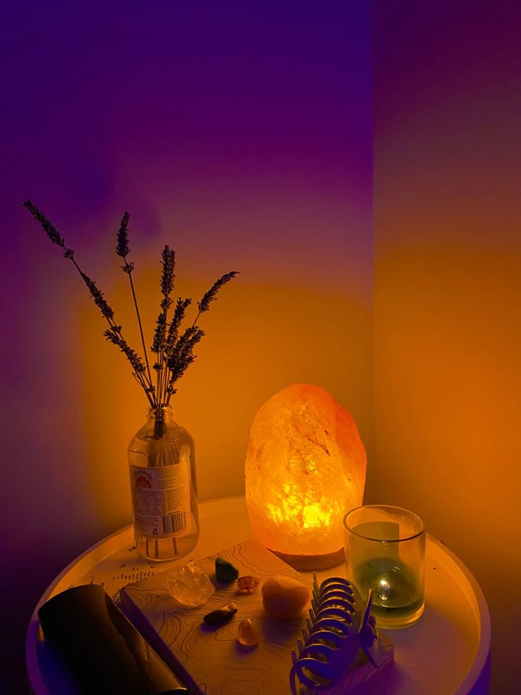 a table topped with a vase filled with flowers next to a lit candle and book