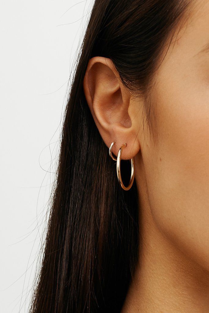 a close up of a person wearing a pair of gold hoop earrings on their ear