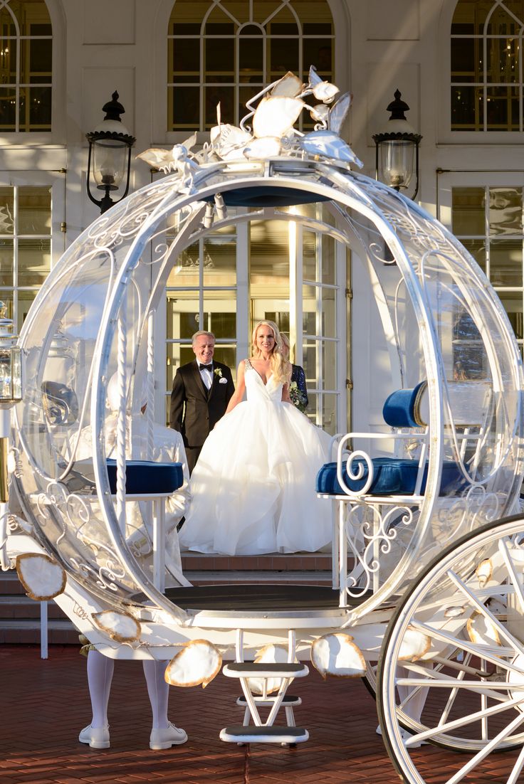 a bride and groom standing in front of a white horse drawn carriage with blue seats