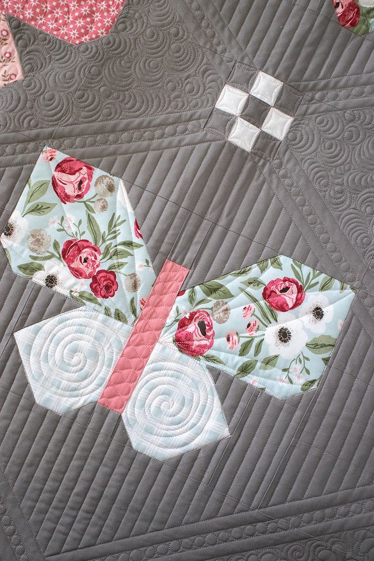 a quilted table topper with flowers and squares in the center, on a gray background