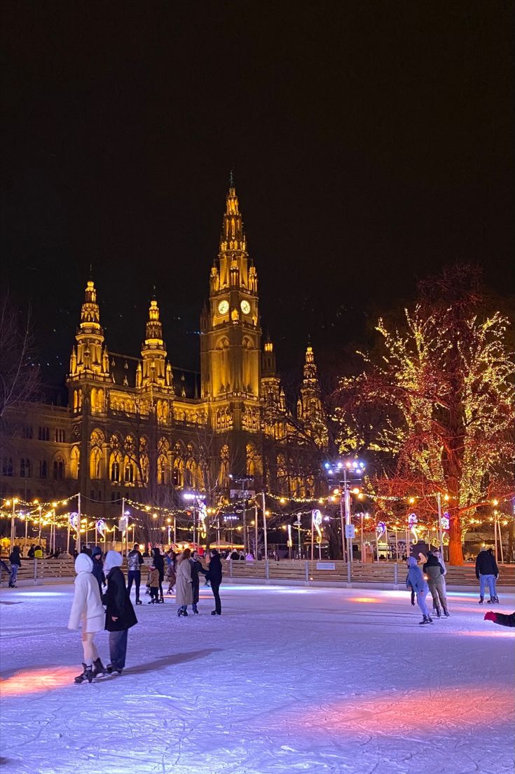 people skating on an ice rink at night in front of a large building with lights