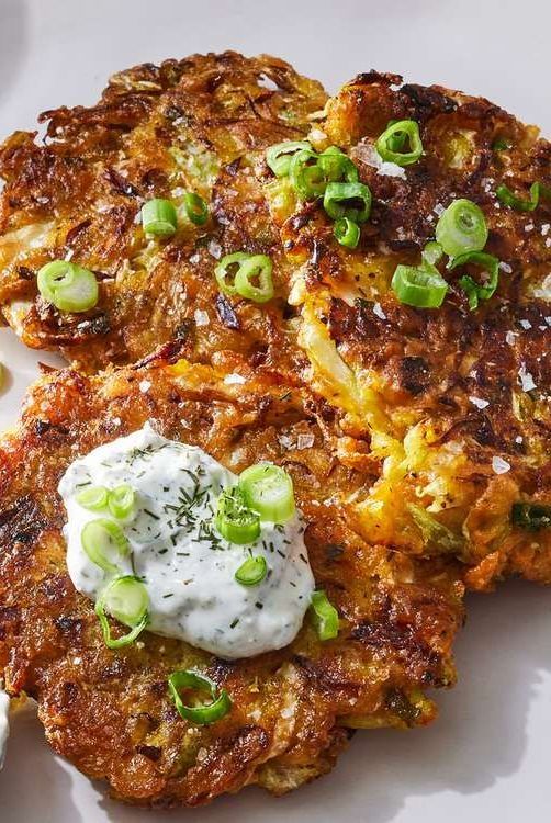 two crab cakes with sour cream and scallions on a white plate, ready to be eaten