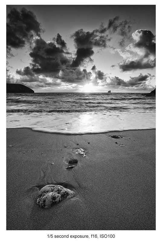 two rocks on the beach with clouds in the background