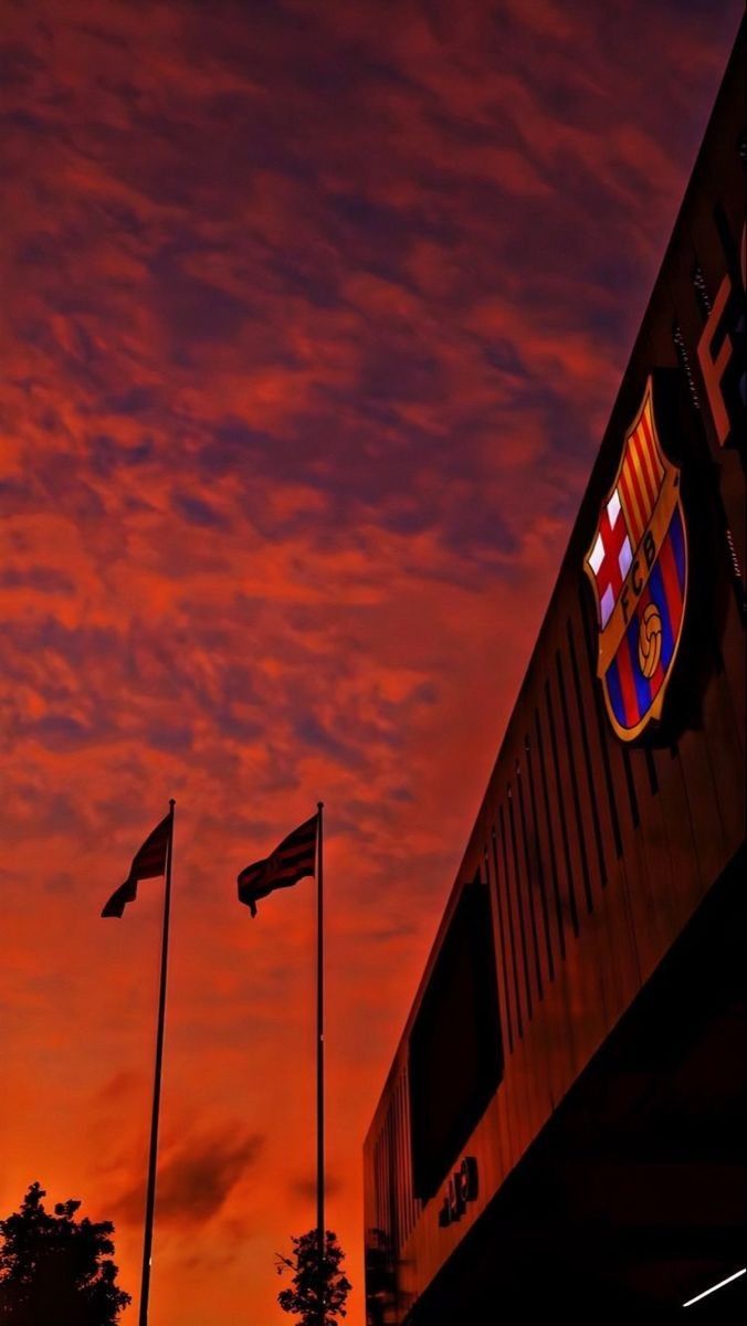 the sun is setting behind some flags on poles in front of an orange and blue sky