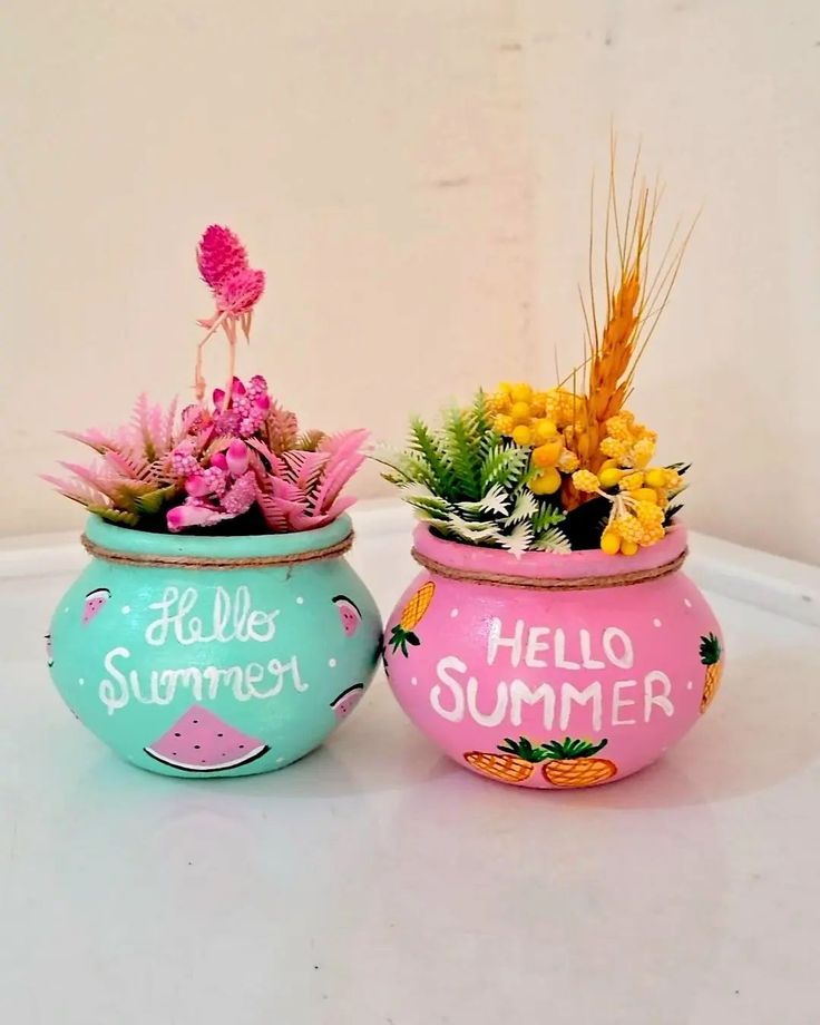 two pots with flowers and plants in them on a white counter top, one has hello summer written on it