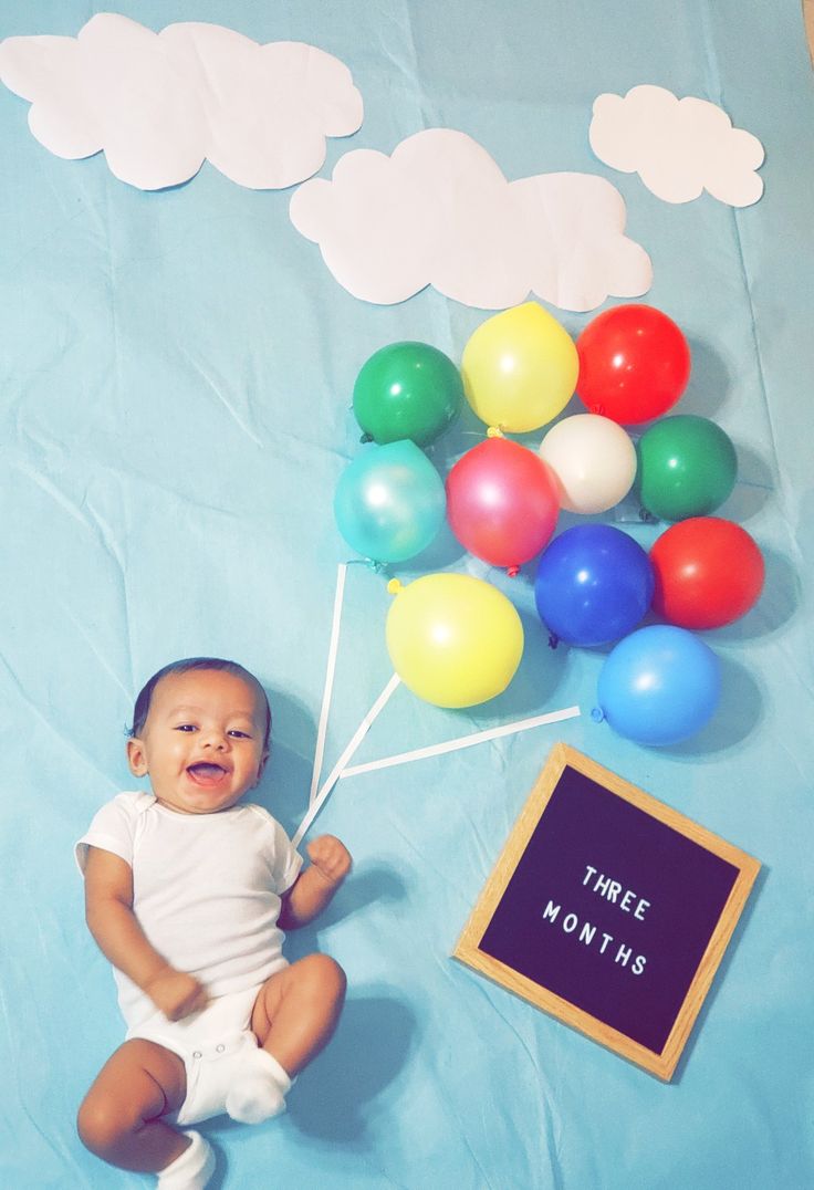 a baby sitting on the ground with balloons and a chalkboard in front of it