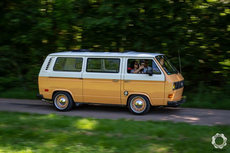 an orange and white van driving down a road with trees in the backround