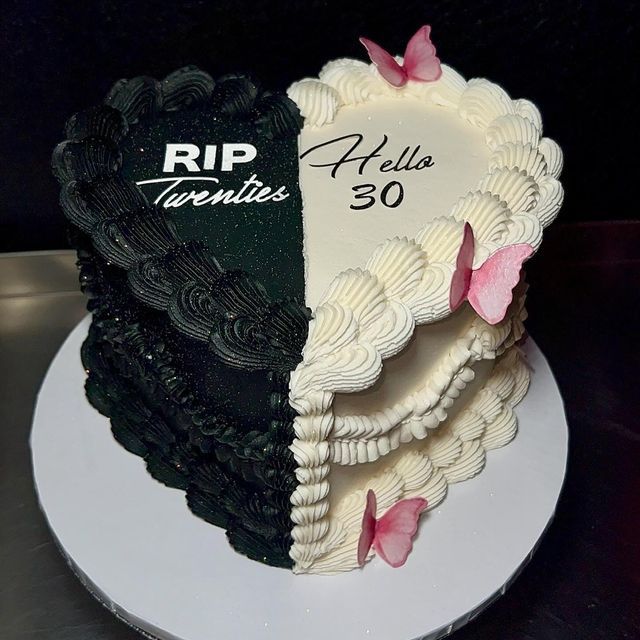 a black and white cake with pink butterflies on it's side, in the shape of a heart