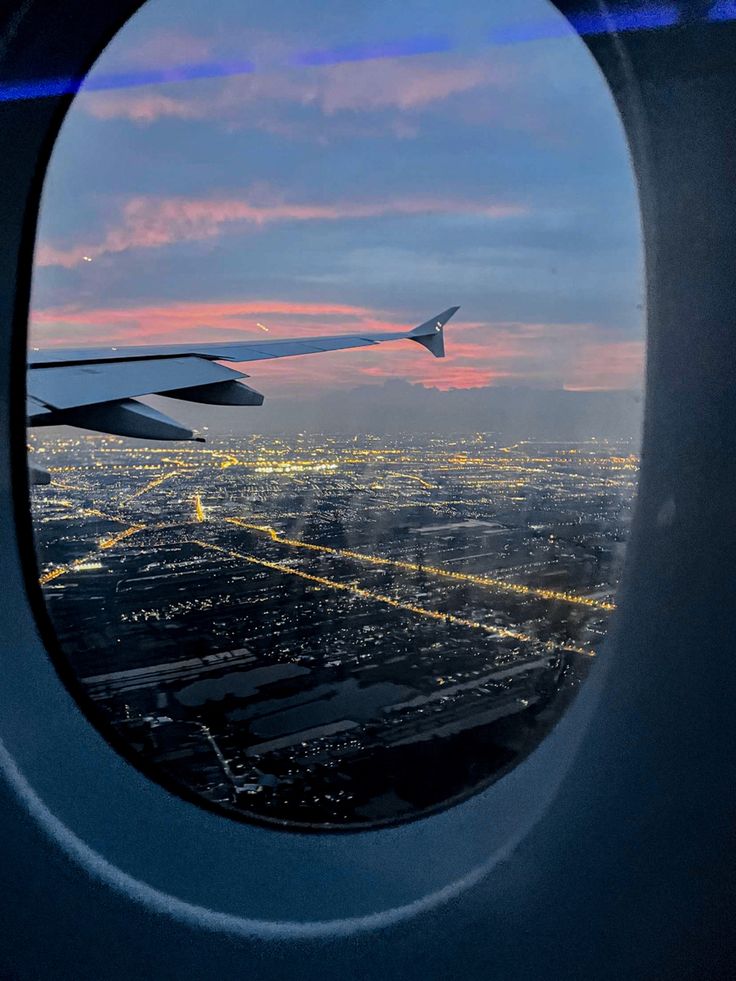 an airplane window looking out at the city lights and sky from inside another plane's wing