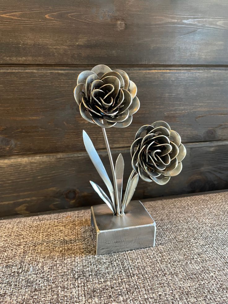 two metal flowers are in a silver vase