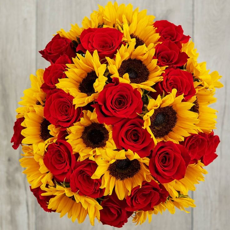 a bouquet of sunflowers and red roses in front of a white wooden background