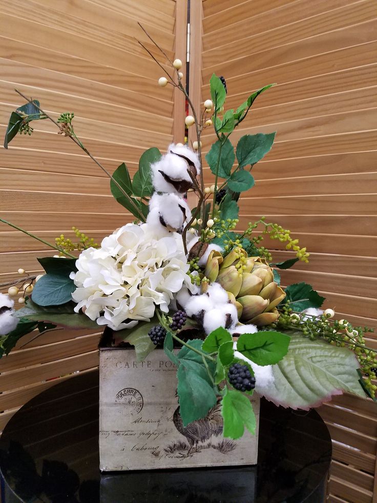 a vase filled with white and green flowers on top of a black table next to a wooden wall