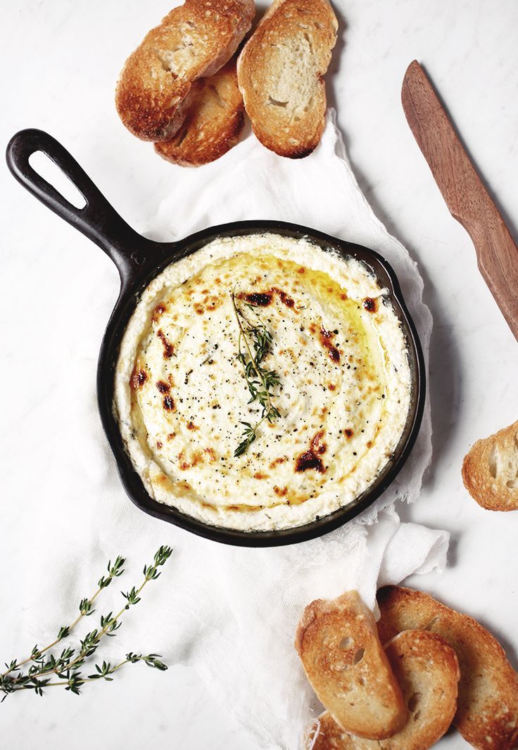 a pan filled with dip and bread on top of a white cloth next to some croissants