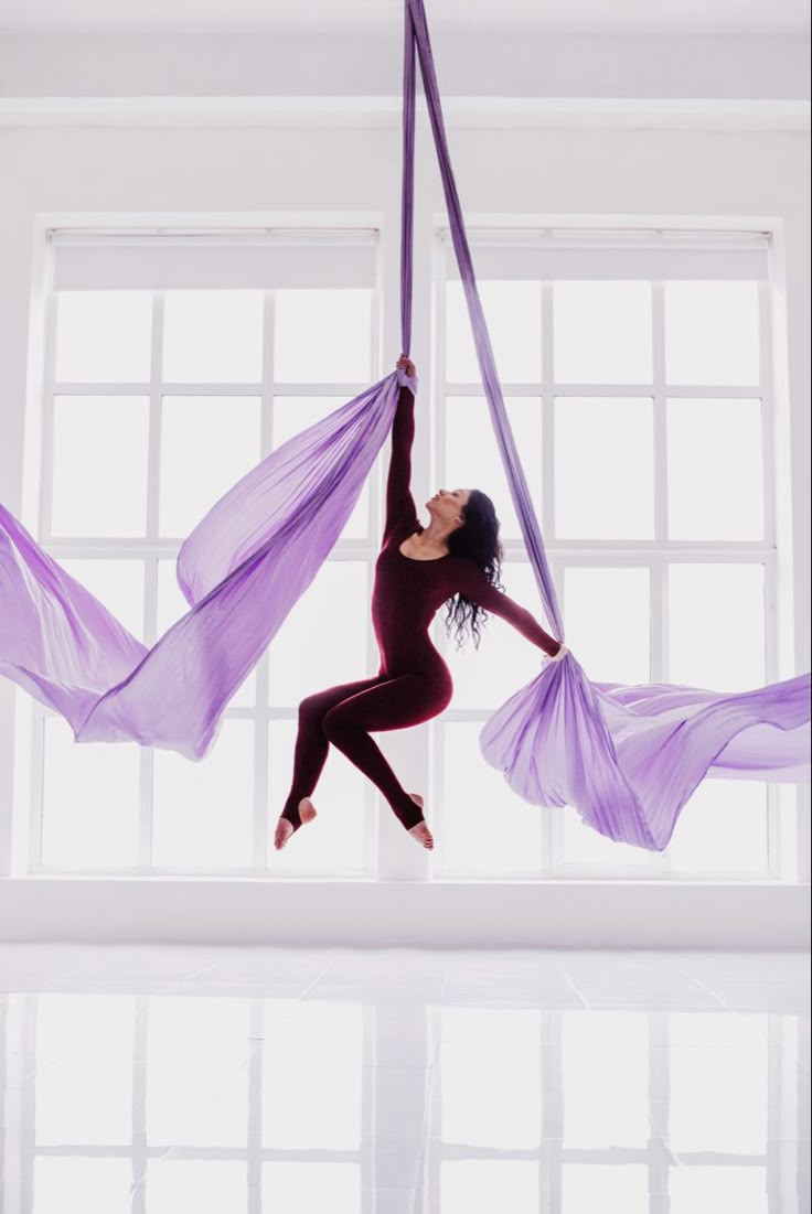 a woman is doing aerial acrobatics with purple fabric