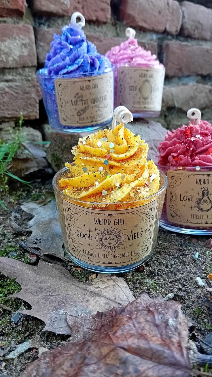 three jars filled with different colored candies sitting on top of the ground next to a brick wall