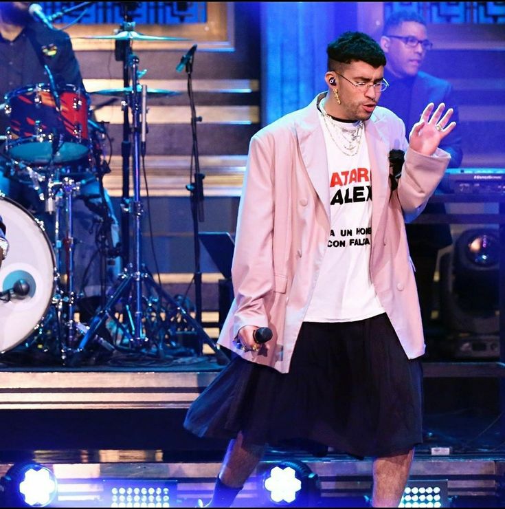 a man in a pink jacket and black skirt standing on stage with his hands up