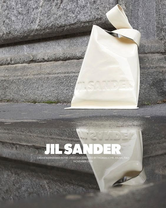 a white bag sitting on the ground next to a stone wall with its reflection in it