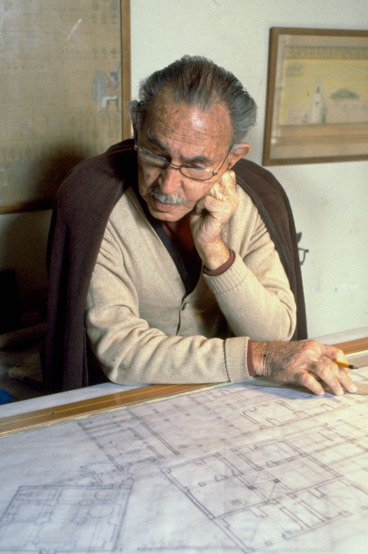 an older man sitting at a table with blueprints on it