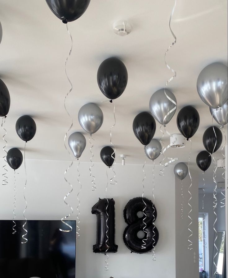 balloons and streamers are hanging from the ceiling in this room with black and silver decorations