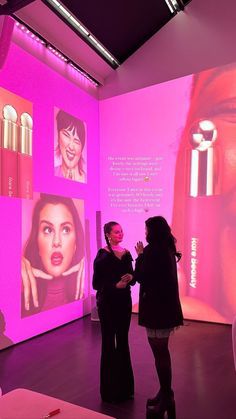 two women standing in front of a pink wall with lipstick on it and pictures behind them