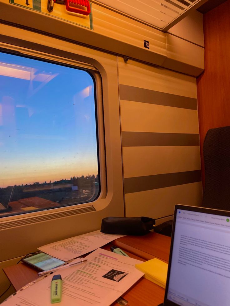 a laptop computer sitting on top of a wooden desk next to a window with a view of the city