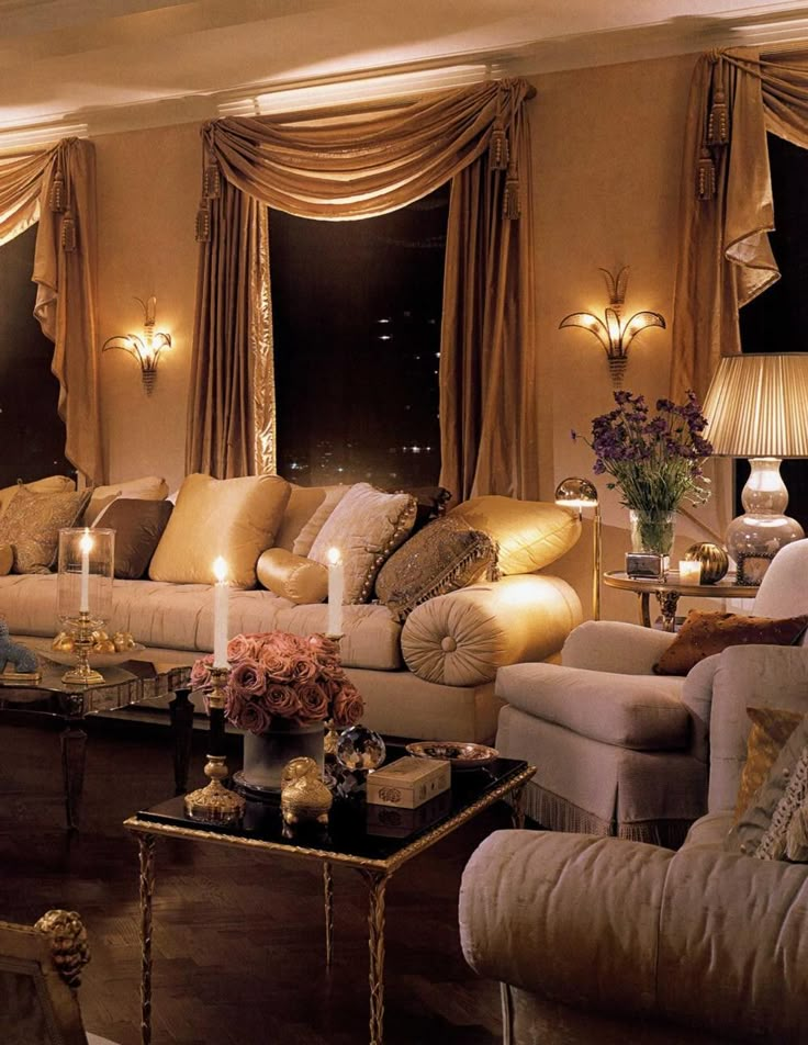 a living room filled with lots of furniture next to tall windows covered in gold curtains