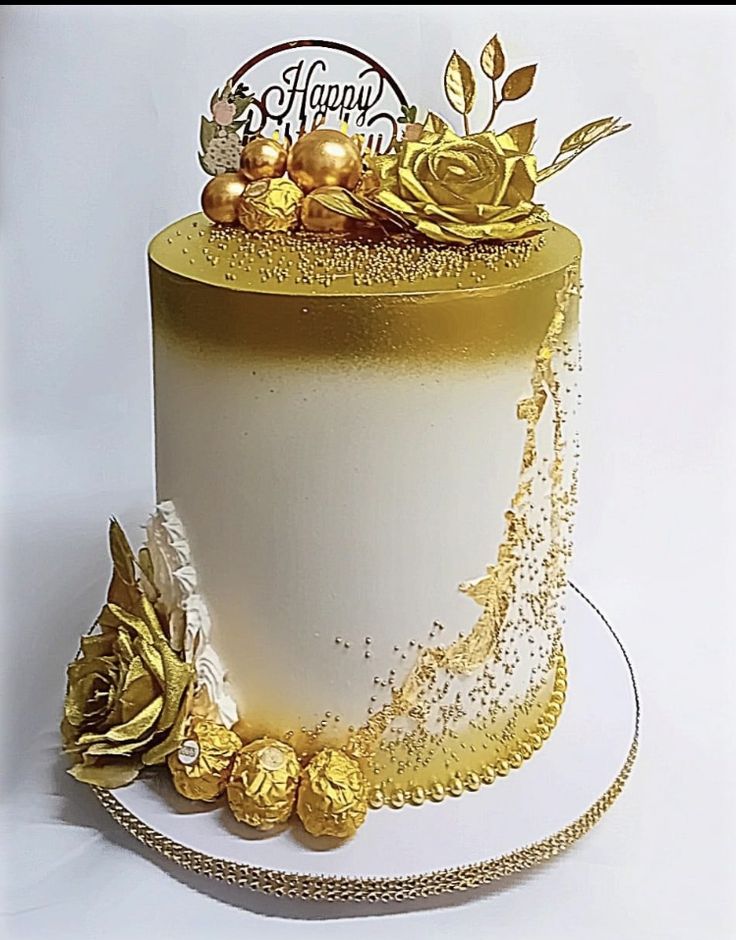 a white and gold decorated cake with flowers on the top is sitting on a plate