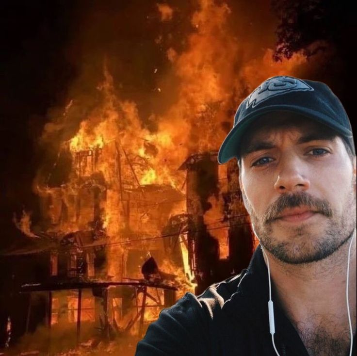 a man wearing headphones standing in front of a house on fire with an image of a burning building behind him