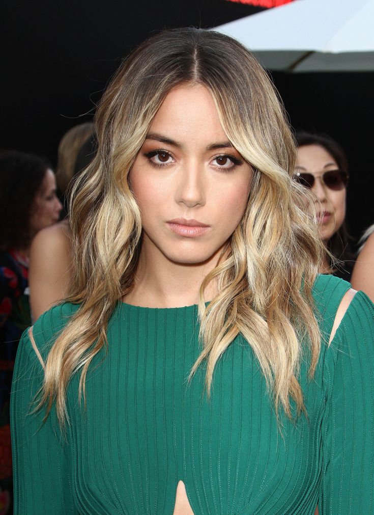 a woman with blonde hair and green top looking at the camera while standing in front of other people